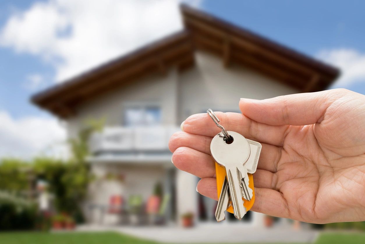 A person holding keys in front of their house.