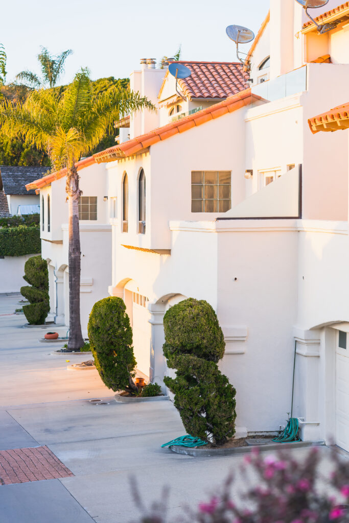 Beautiful houses with nicely landscaped front the yard, and green hills and clear blue sky in the background in a small beach town in California at sunset